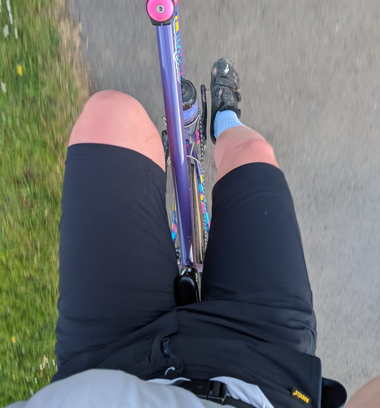 View down at a rider's legs in black Overland Selector shorts, pedalling a purple patterned bike.