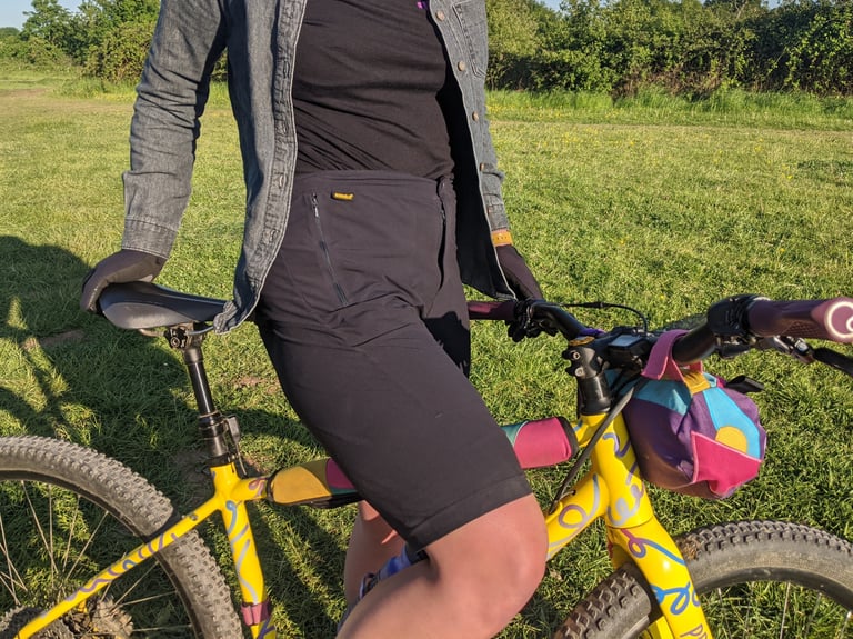 Zipped side pocket of the Overland Selector shorts, worn astride a yellow hardtail with a colourful handlebar bag.