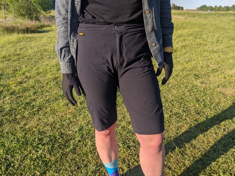 Reviewer wearing the Overland Selector shorts, standing on grass in evening sun with a denim shirt and gloves.