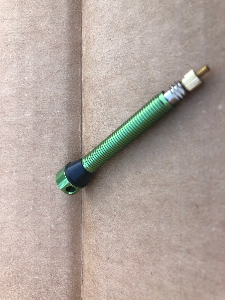 Green anodised CushCore side-exit tubeless valve with a black rubber base lying on cardboard.