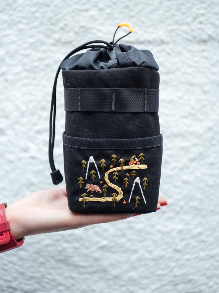 Wizard Works Voila! snack bag in black waxed canvas, embroidered with a winding trail, a bear and snowy peaks.