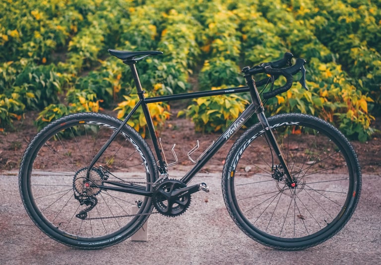 Ivo Azenha's black Fearless Vulture with a Shimano 105 crankset, stood on a path in front of a crop field.