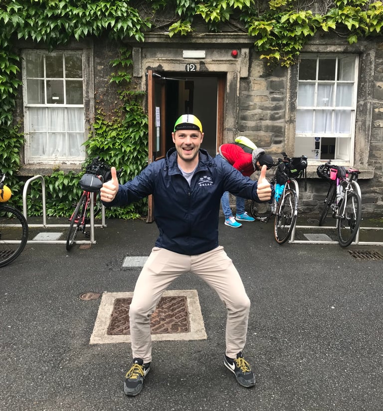 Smiling rider in a TransAtlantic Way cap gives two thumbs up outside the Trinity College Dublin rider briefing.