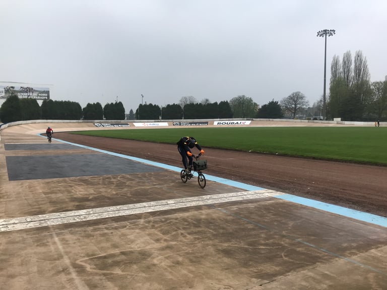 Rider on a Brompton with a front bag rides the banked Roubaix velodrome during TransAtlantic Way training.
