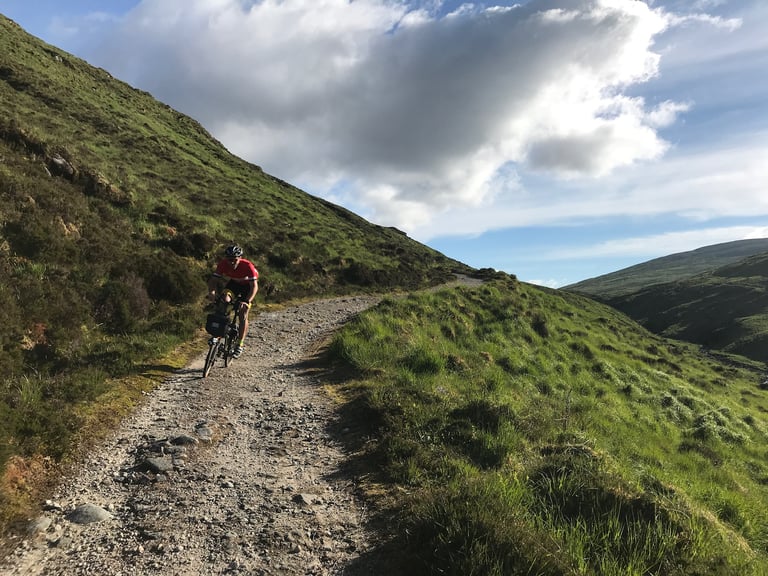 Rider on a loaded Brompton rides a rocky gravel track along a hillside in Donegal during the TransAtlantic Way.