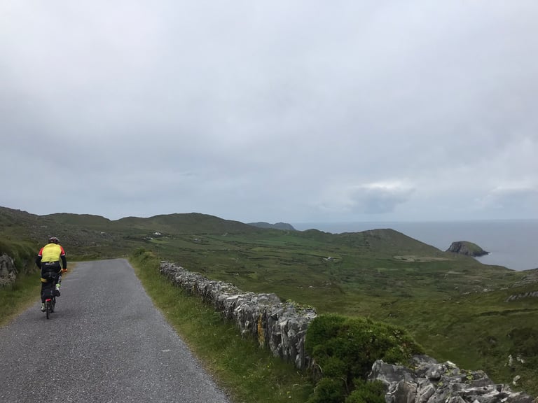 Brompton rider climbs a quiet lane past a drystone wall above the rugged West Cork coast on the TransAtlantic Way.