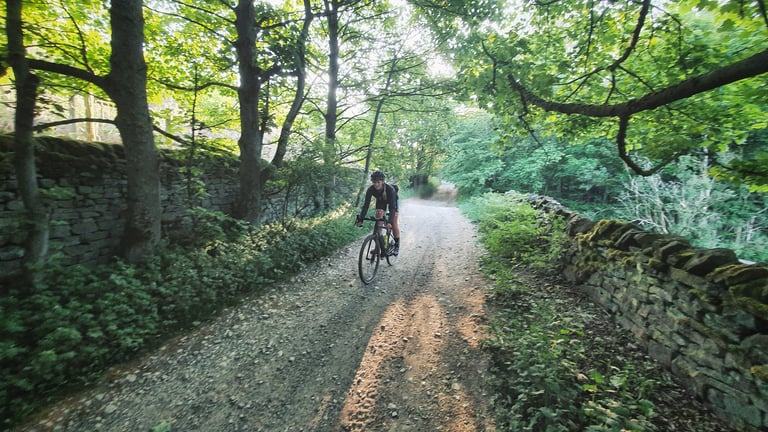 Rider on a shaded gravel track between mossy stone walls and trees at the cold 6am start of the Dirty Kanzelled.