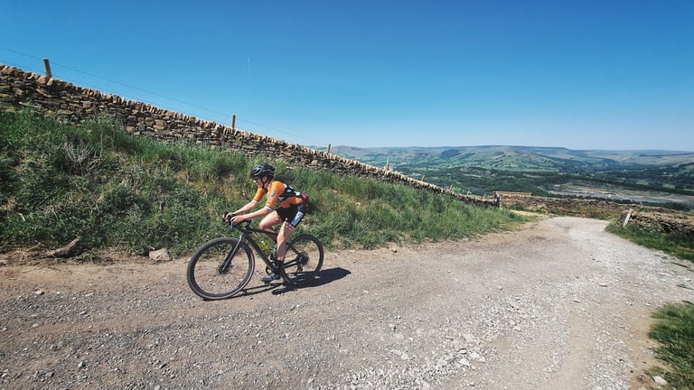 Rider in orange kit on a stony gravel track with the Derbyshire hills and valley behind on the Dirty Kanzelled.