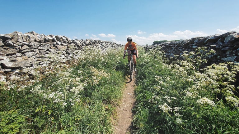 Magspeed rider on a narrow singletrack between drystone walls and cow parsley on the Peak District gravel route.