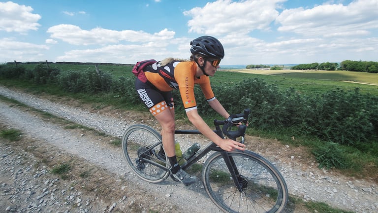 Rider in orange Magspeed Racing kit on a Specialized Diverge gravel bike, riding a stony Peak District track.