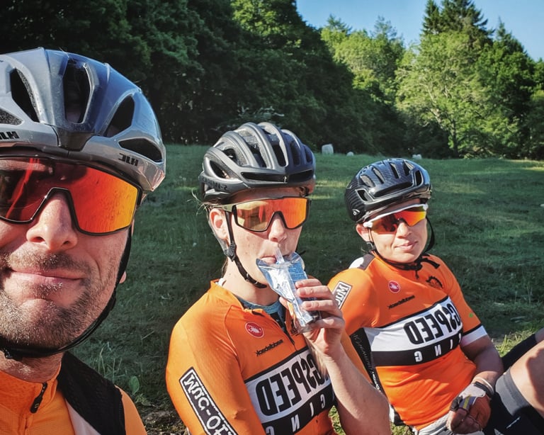 Selfie of three Magspeed Racing riders in orange kit and helmets resting on grass after the Dirty Kanzelled.