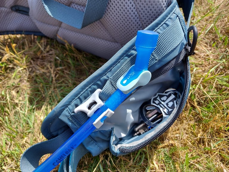 Repack LR 4 bite valve and hose held in a belt clip beside an open zipped pocket holding keys.