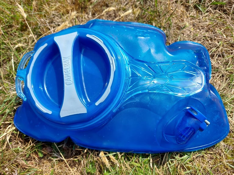 Blue Camelbak Crux reservoir with handle in the filler cap, removed from the Repack LR 4 and lying on grass.
