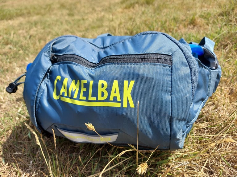 Front of the Camelbak Repack LR 4 in blue with yellow logo, zipped pocket and reflective loop at the base.