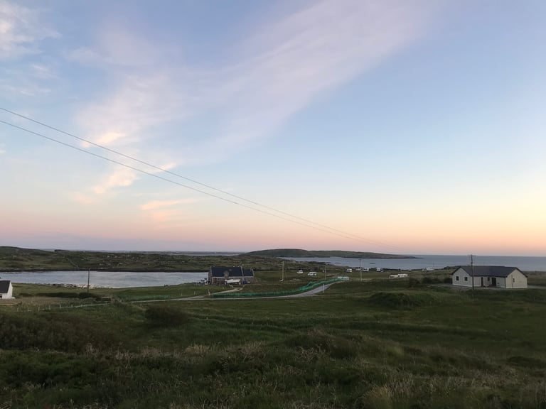 Sunset over the Connemara coastline, with cottages and a campsite by the water, on the TransAtlantic Way route.
