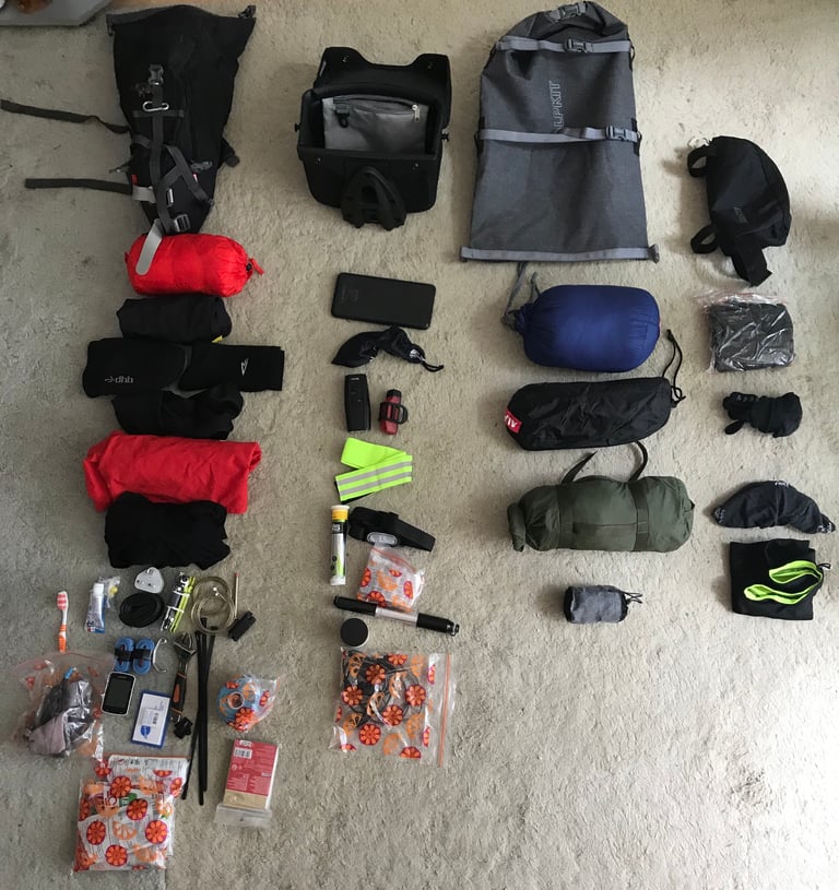 Kit grid of bikepacking gear laid out on a carpet: Alpkit bags, sleeping bag, shelter, clothing, lights, tools and spares.