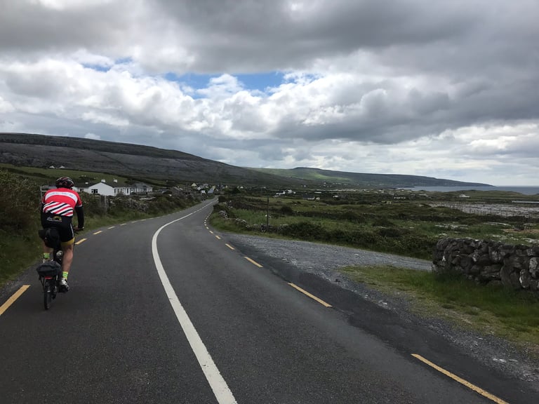 Brompton rider on a coastal road past stone walls and white cottages during the TransAtlantic Way Race.