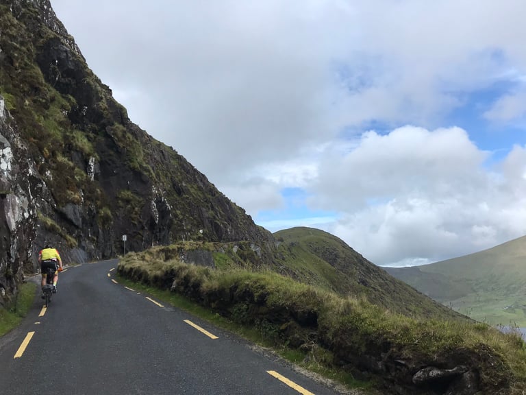Rider on a Brompton climbs a road cut into a steep rock face on the Dingle Peninsula, TransAtlantic Way Race.