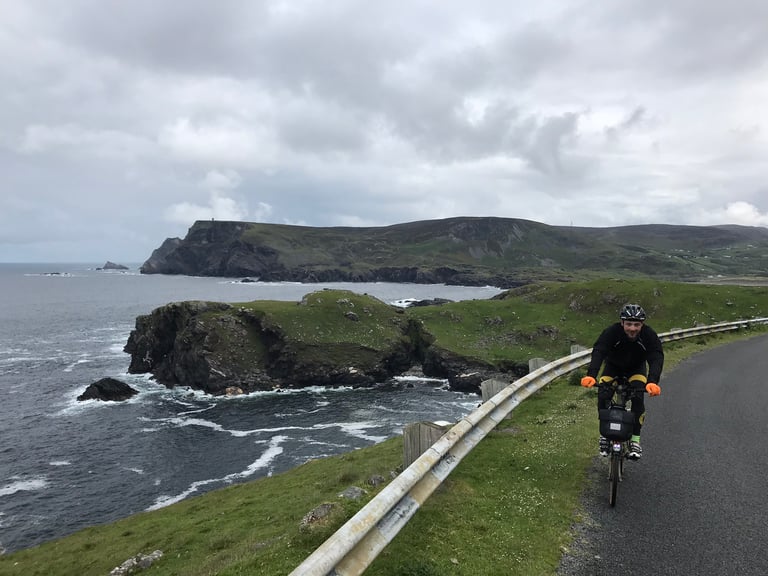 Rider in orange gloves climbs a sea-cliff road on a Brompton during the TransAtlantic Way Race in Ireland.