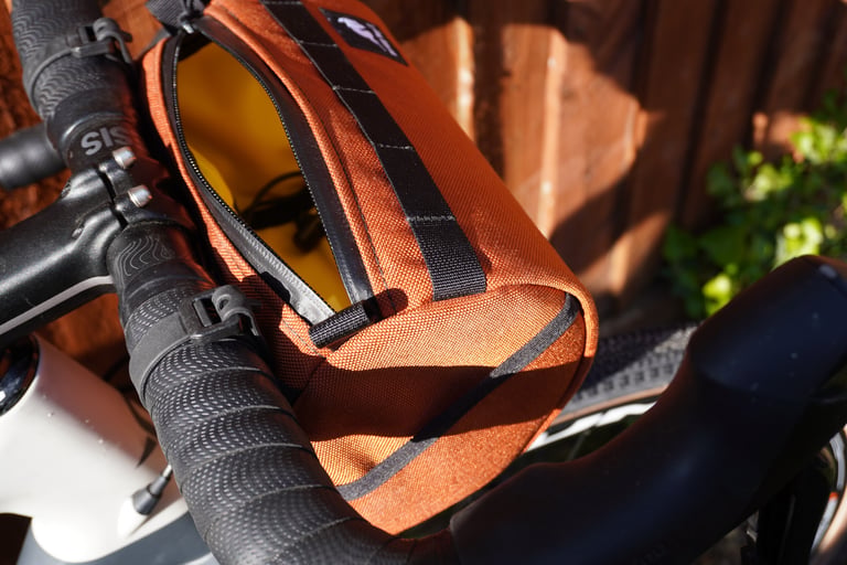 Wizard Works Lil Presto! in rust on a handlebar with its water-resistant zip open, showing the yellow liner.