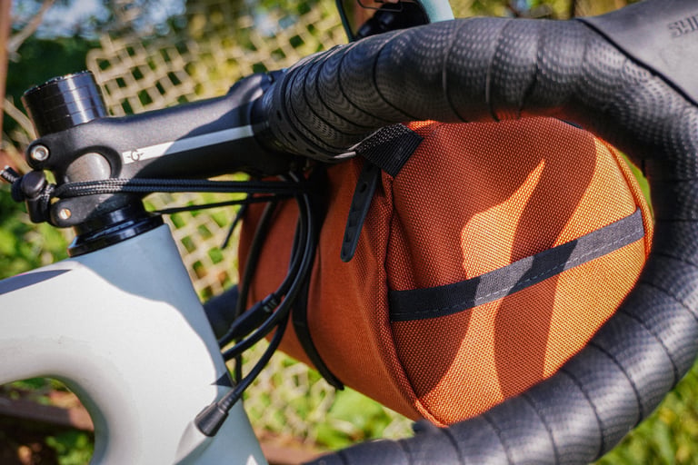 Side view of the Lil Presto! barrel bag held to the bars by rubber straps beside the stem and cables.