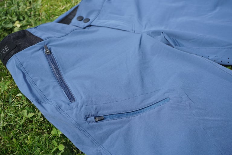 GORE C5 shorts laid on grass showing the zipped hip pocket and smaller zipped pocket on the lower right leg.