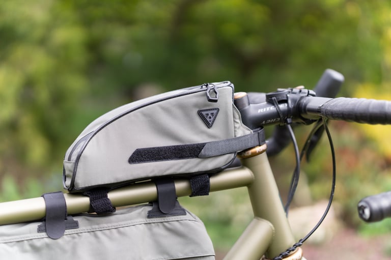 Topeak Toploader on the top tube of a green gravel bike, held by Velcro straps behind the stem.
