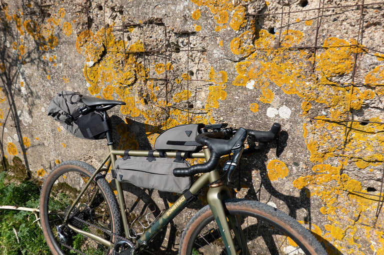 Bombtrack Hook EXT with Topeak Toploader, Midloader and Backloader fitted, leaning on a lichen-covered wall.