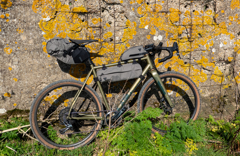 Olive Topeak bags colour-matched to the Bombtrack Hook EXT frame, parked side on against a lichen-covered wall.