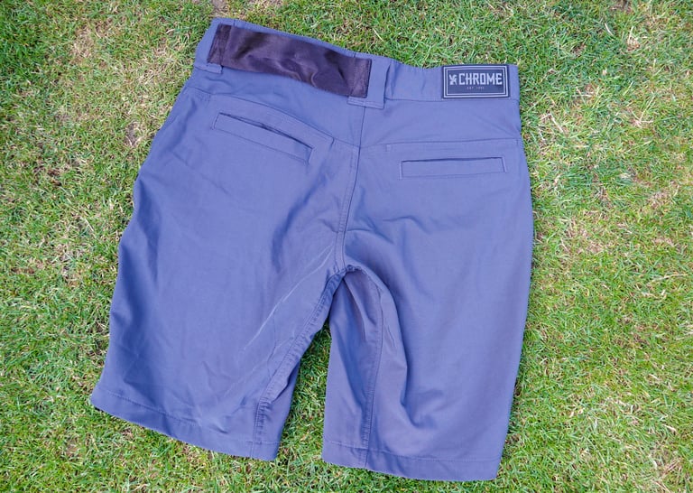 Chrome Industries Folsom Short 2.0 laid on grass, rear view, showing the seatbelt webbing U-lock holder and two back pockets.