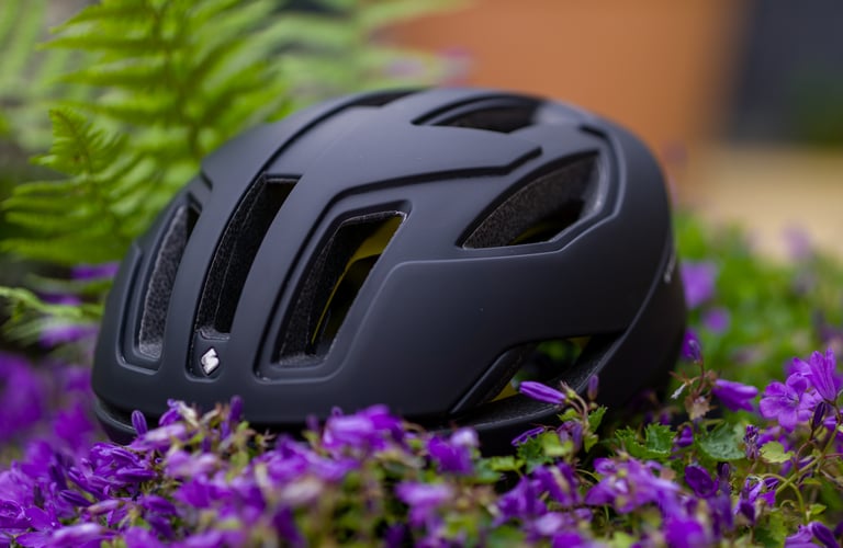 Front of the matte black Falconer II MIPS helmet, with its long vents above the brow, among purple flowers.