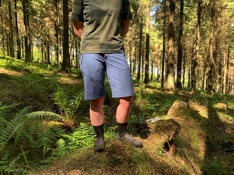 Front view of the GORE C5 Women's Shorts worn with a green T-shirt in sunlit woodland, three zipped pockets in view.