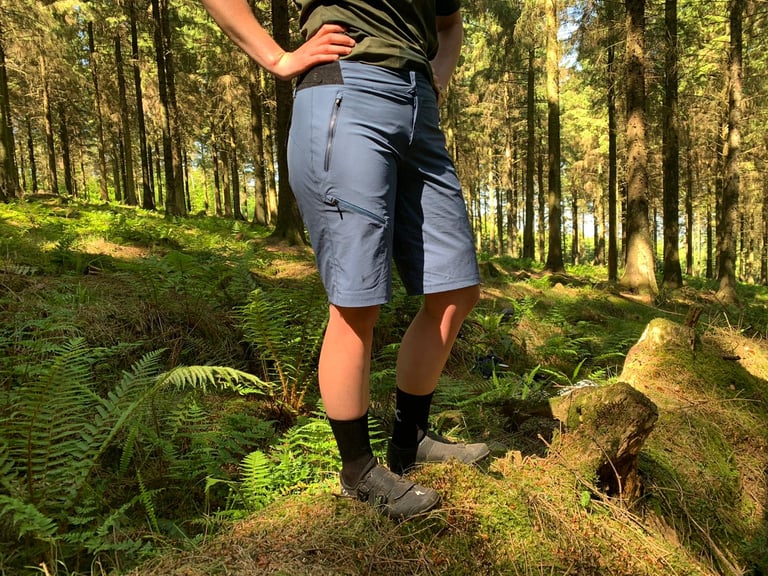 Rider in the GORE C5 Women's Shorts and clip-in shoes among ferns, showing how far the hem sits above the knee.