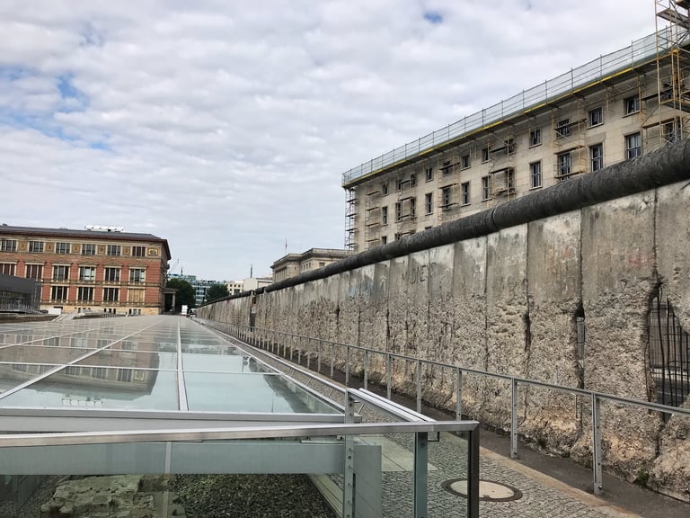Surviving section of the Berlin Wall, chipped and graffitied, beside a glass-covered excavation in Berlin.