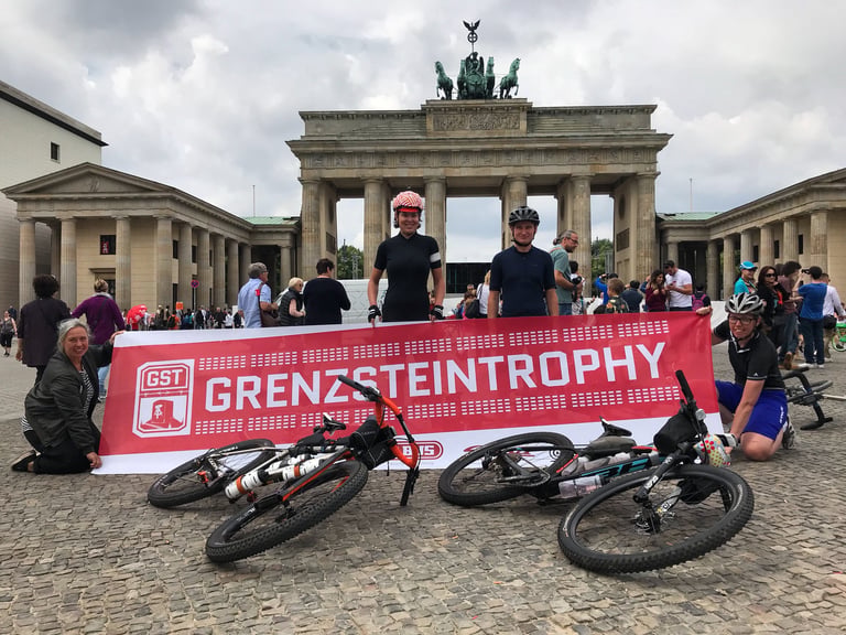 Riders and bikes with a Grenzsteintrophy banner in front of the Brandenburg Gate in Berlin at the prologue start.
