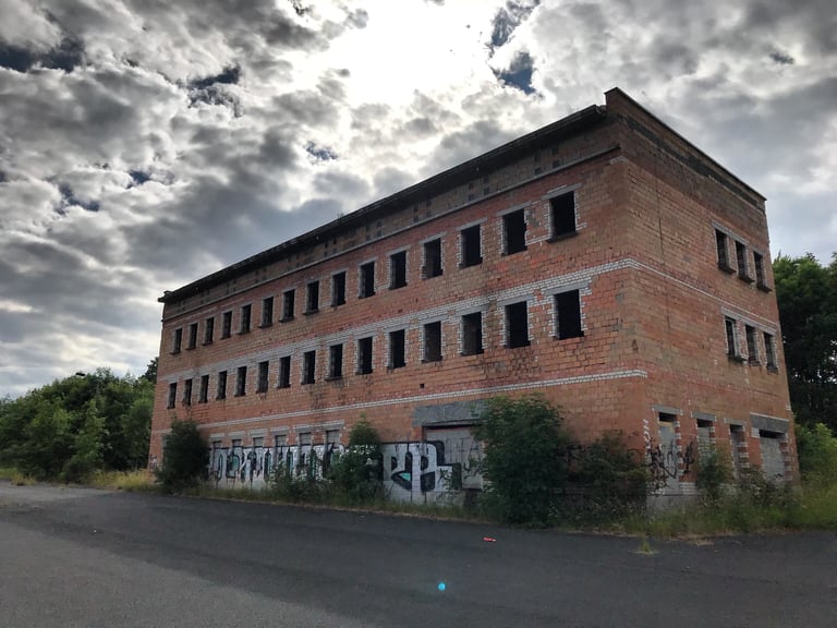 Derelict red-brick former Russian barracks with empty windows and graffiti at Henneberg, Germany.