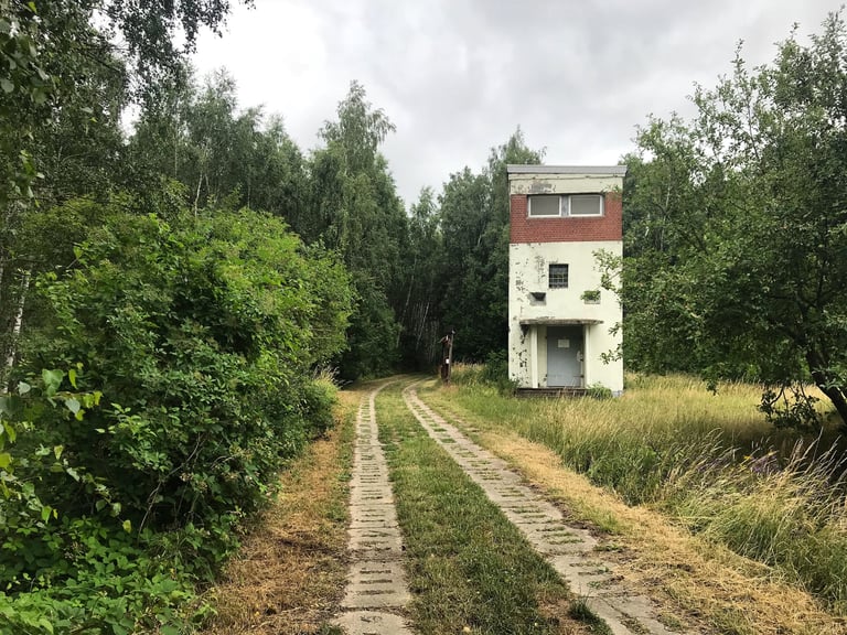 Old East German watchtower beside a panzer plate track through woods on the former inner German border.