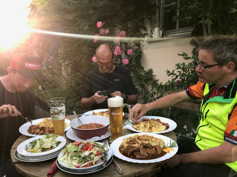 Three riders eat pasta and beef stew in a pub garden with beer after a day on the Grenzsteintrophy.