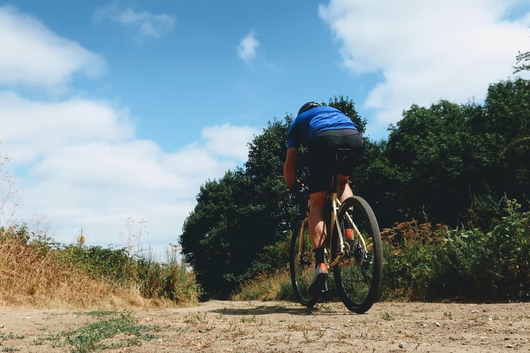 Rider in a blue jersey rides away on a cream Fearless Vulture along a dry gravel track lined with trees.