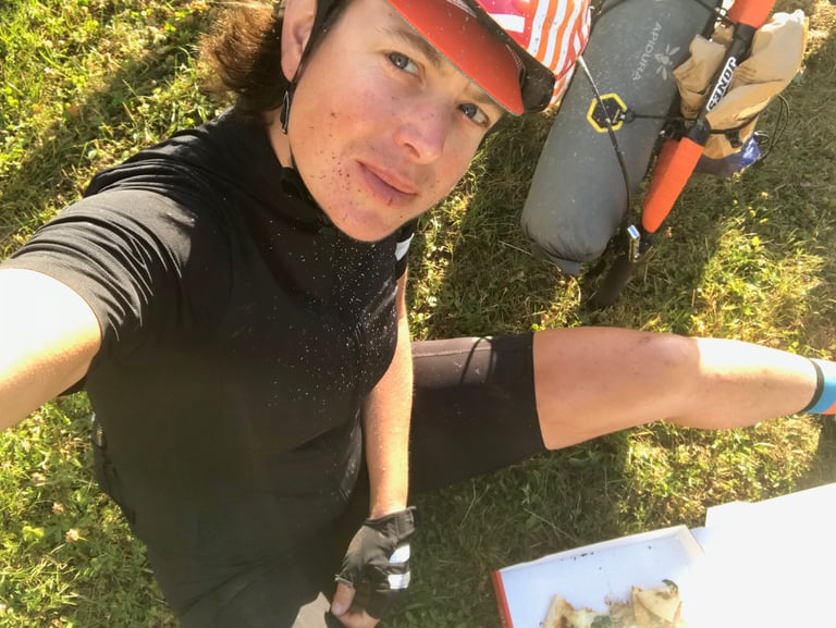 Emma Osenton takes a selfie sitting on the grass beside a pizza box and her loaded bike on the Grenzsteintrophy.