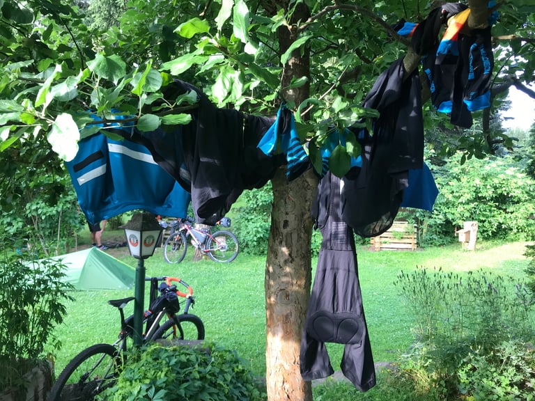 Cycling kit hung to dry in a tree beside a campsite, with a tent and bikes behind, on the Grenzsteintrophy.