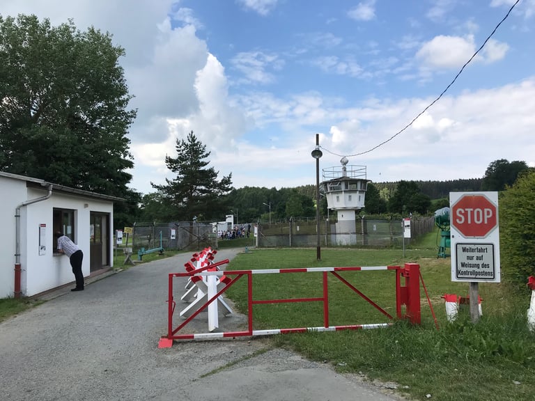 Former border checkpoint at the Mödlareuth Grenze museum, with a watchtower, barrier and red stop sign.