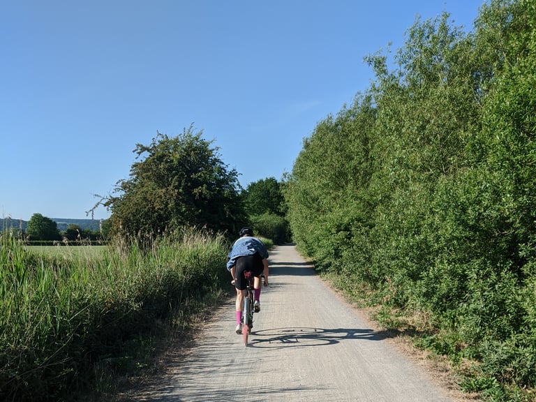Rider in a blue top on the flat, light-gravel Strawberry Line cycle path between hedges in Somerset.