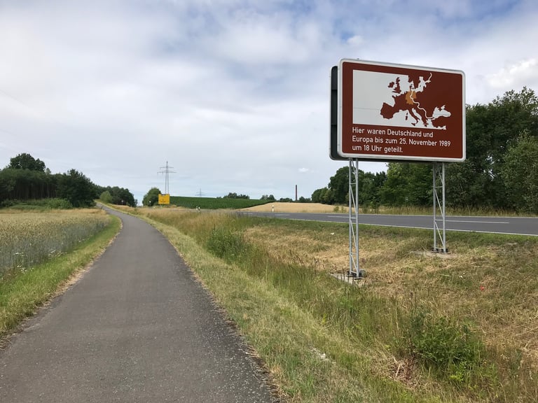 Brown sign beside a cycle path marking where Germany and Europe were divided until 25 November 1989.