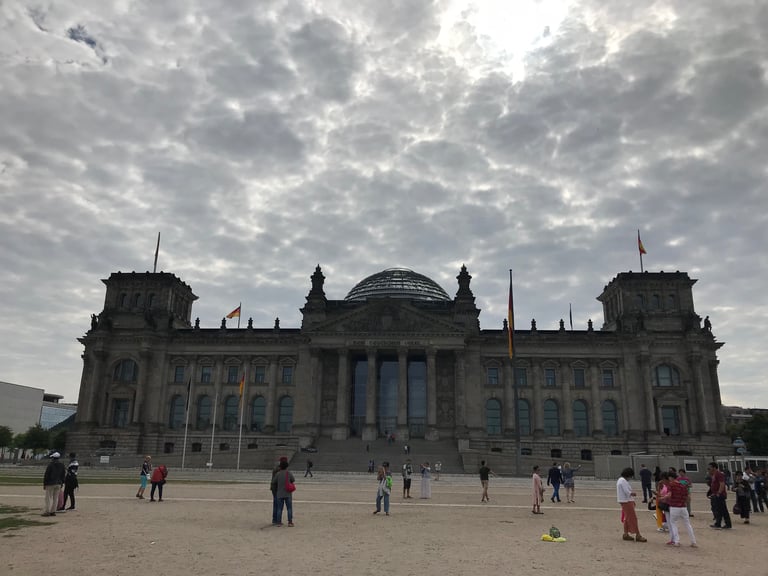 The Reichstag building in Berlin under a cloudy sky, with visitors in the foreground.