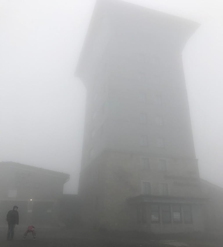 Tower on the Brocken summit lost in thick fog, two walkers at its base, near the former Russian listening station.