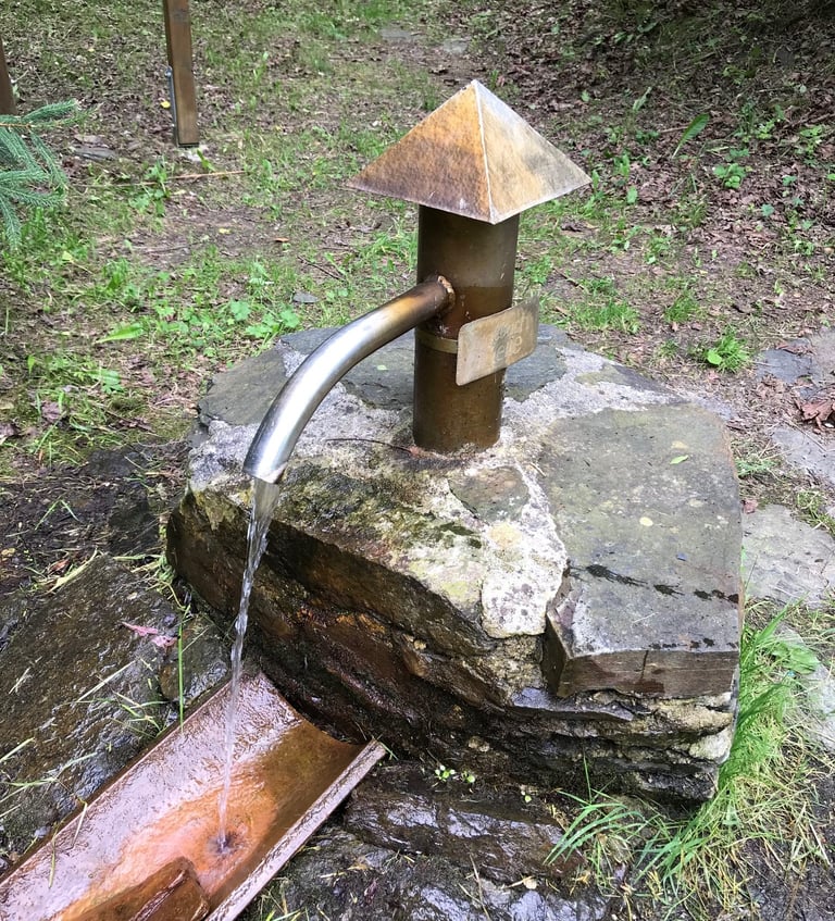 Metal water spout with a pyramid cap on a stone block in woodland, found on the Grenzsteintrophy route.