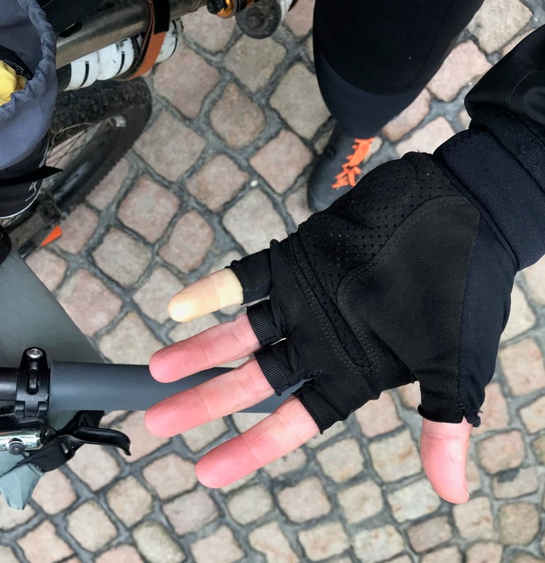 Gloved hand held out beside a bike handlebar on cobbles, one fingertip pale from the cold, during the Grenzsteintrophy.