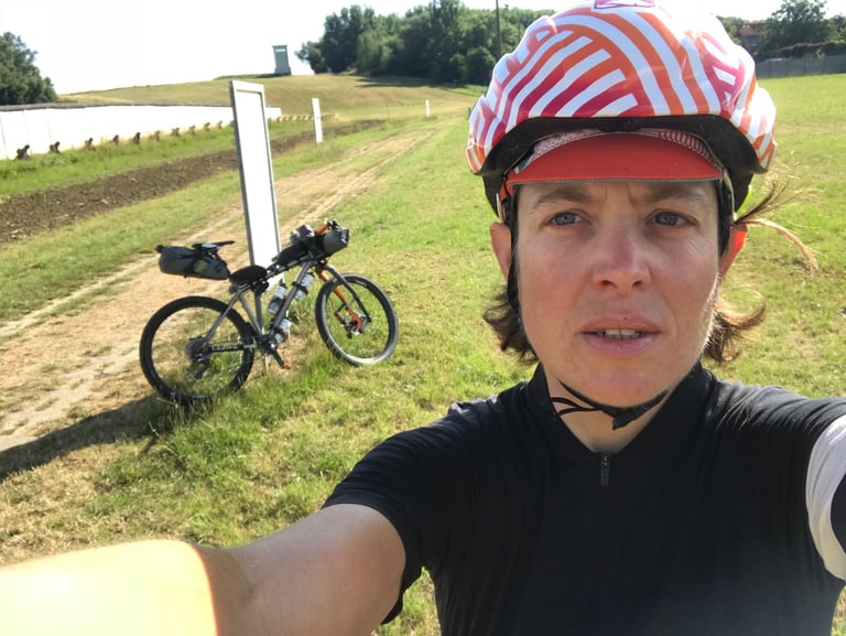Emma Osenton takes a selfie beside her loaded Kinesis mountain bike at the Hötensleben border museum wall.