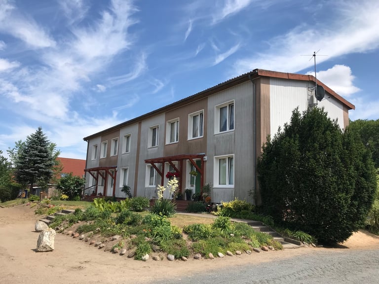Two-storey East German terraced housing with plain cladding and a tidy garden near the Grenzsteintrophy route.